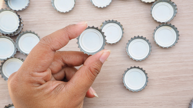 A hand holding a bottle cap over a pile of more bottle caps