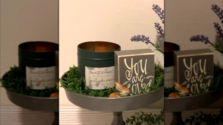 A rustic cake pan turned into a tiered countertop accessory with faux greenery, a candle, and decor accents