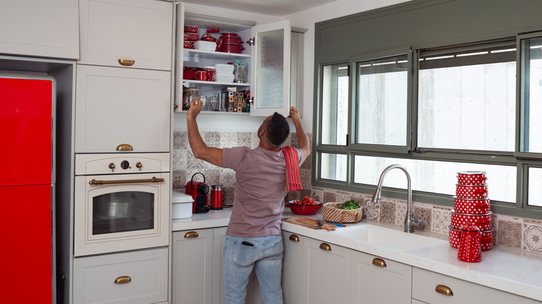 person standing in kitchen opening cabinets