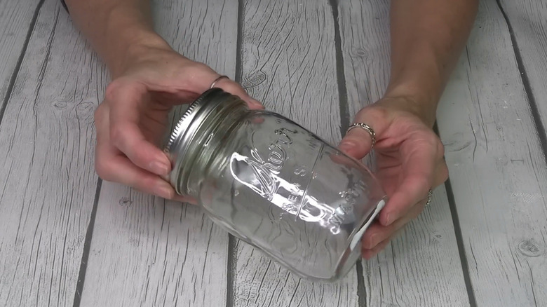 Hands holding an empty mason jar on a wood surface