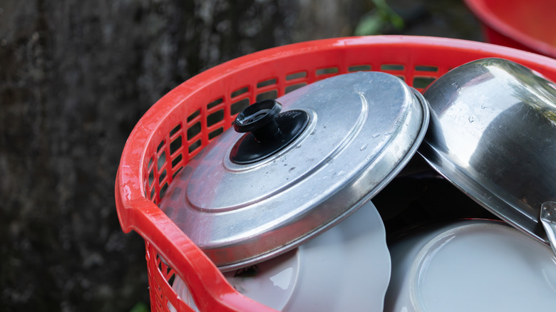 Plates, pots, and pot lids stacked in a plastic basket outside