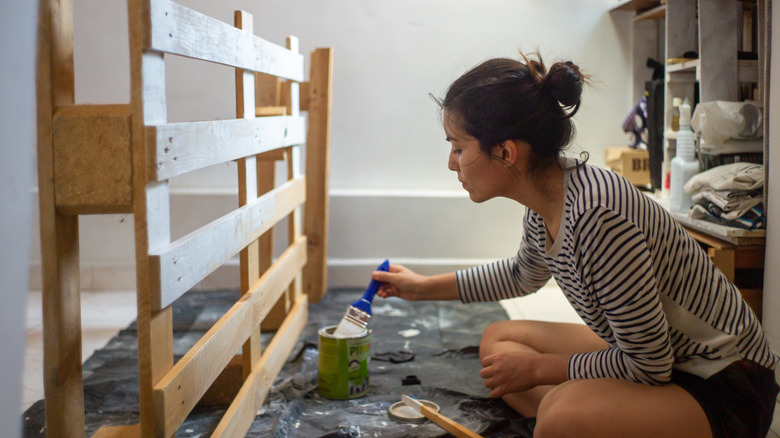 Person painting wood pallet on the floor of their home for a DIY project.