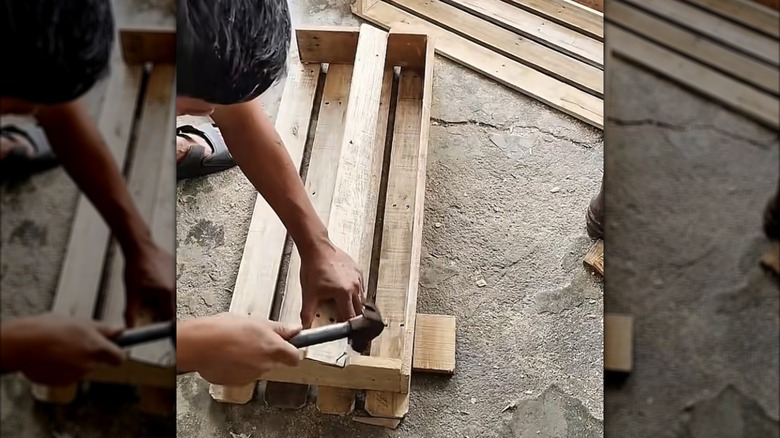 man building a shoe storage compartment out of scrap pallet wood, a hammer, and nails