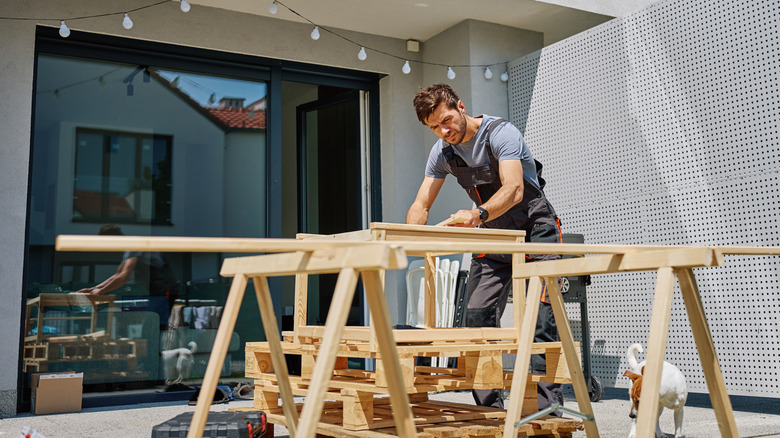Carpenter cutting down pallets on sawhorse on back patio.