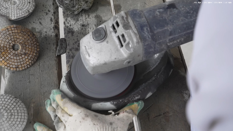 A person polishing a river rock bowl using an angle grinder