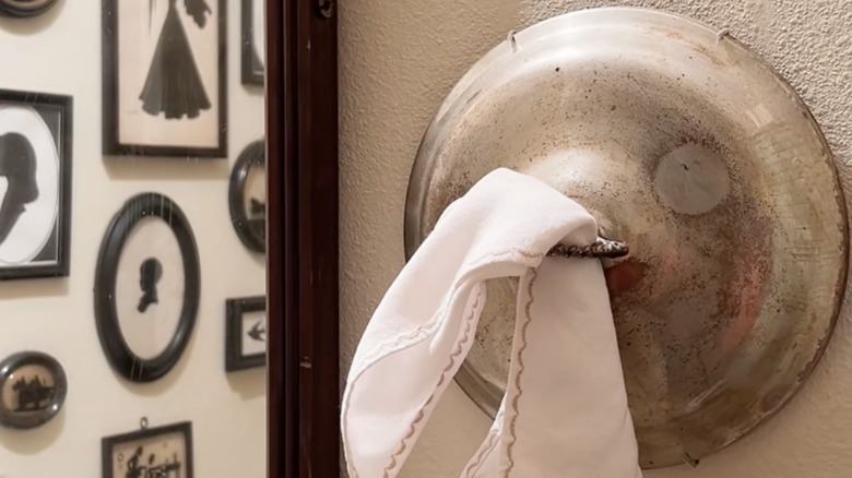 Old pot lid repurposed as wall-mounted bathroom towel holder