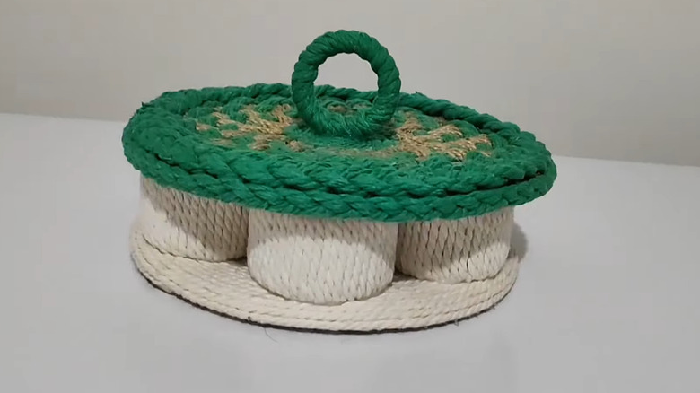 A countertop organizer made of cardboard tubes, decorated with white and green string.