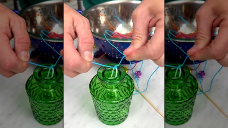 A person's hands tie a blue cord to a wire loop inside a vintage glass jar
