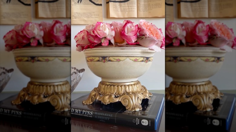 A vintage brass lamp base repurposed as a riser for a vase of flowers