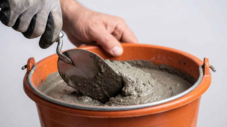 person hand mixing concrete in an orange bucket