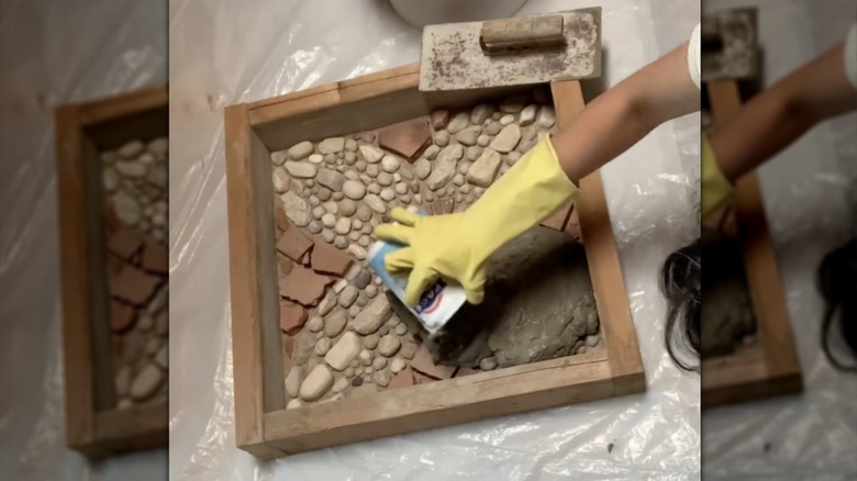 person spreading concrete over a decorative stone pattern in a custom DIY paver