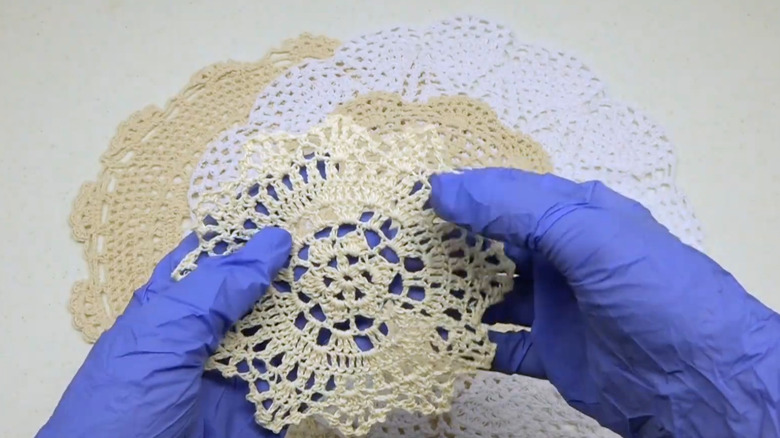 Gloved hands prepare vintage doilies for a DIY project