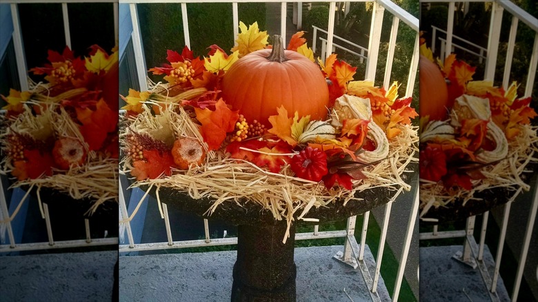 Old birdbath decorated with hay, a pumpkin, and fall leaves