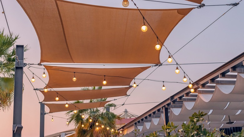 Multiple shade cloths and string lights hanging over a large garden space