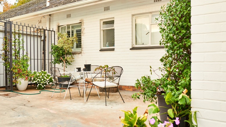 Unshaded concrete patio with metal table and chairs next to cream-colored brick house