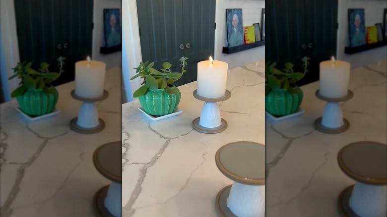 A pillar candle on a white candle stick holder on a marble island