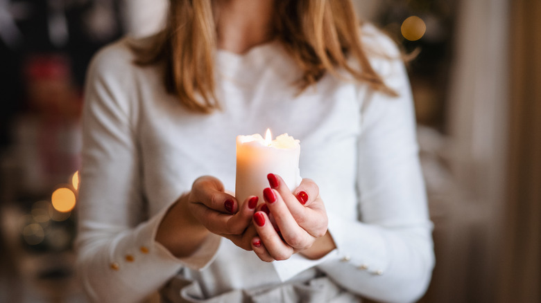 A woman with painted red nails holds a lit candle