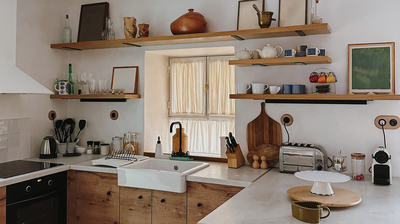 A kitchen with wooden lower cabinets and open shelves on the wall displaying kitchenware