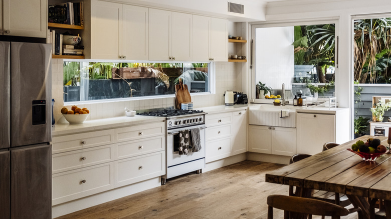A kitchen with white shaker cabinets, wooden flooring, and a wooden dining table