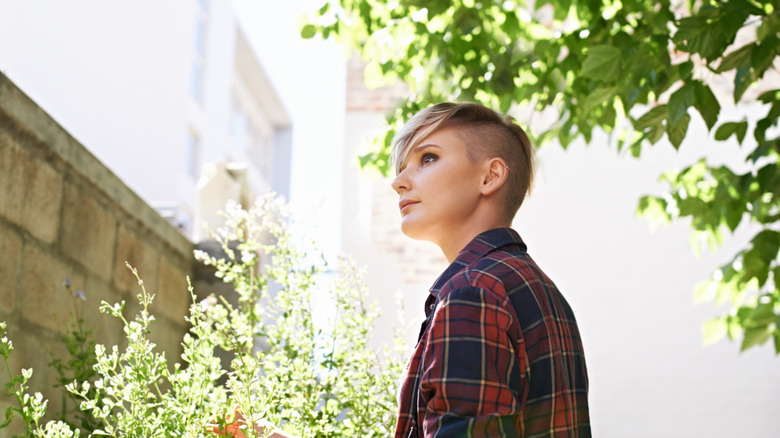 A person stands in their backyard, thinking while surrounded by green foliage