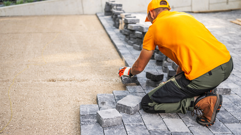 A construction worker laying cobblestone for a patio.