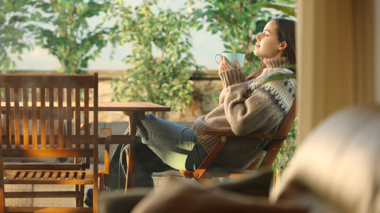 A woman relaxes on her patio, wearing a sweater and drinking from a mug