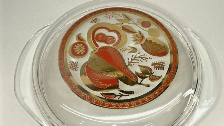 A Paradise burgundy and gold pattern embossed on a glass Pyrex lid fitting a round casserole bowl.