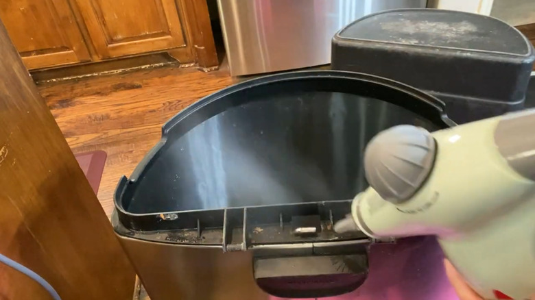 A person cleaning a garbage can with a hand steamer.