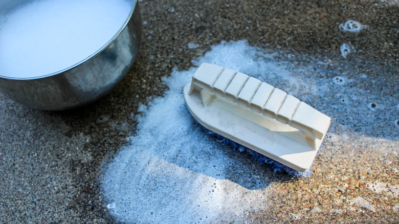 A scrub brush a soapy water on a driveway.