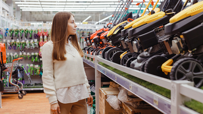 woman in home improvement store looking at lawnmowers on display.