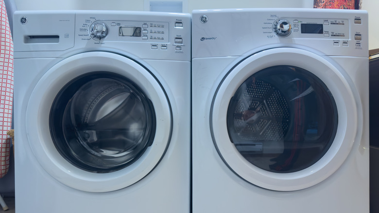 Side-by-side white GE washer and dryer sitting in a laundry room.