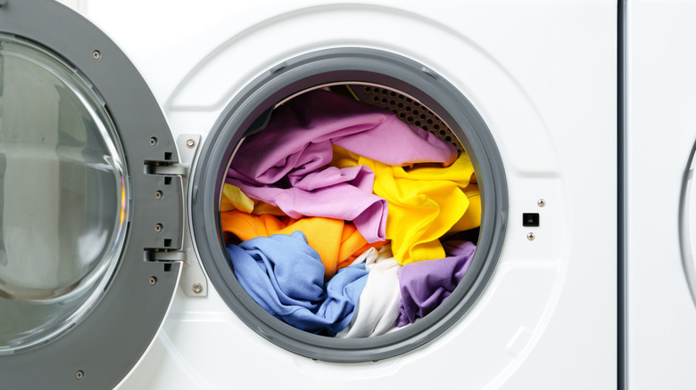 An open washing machine with colorful laundry inside.