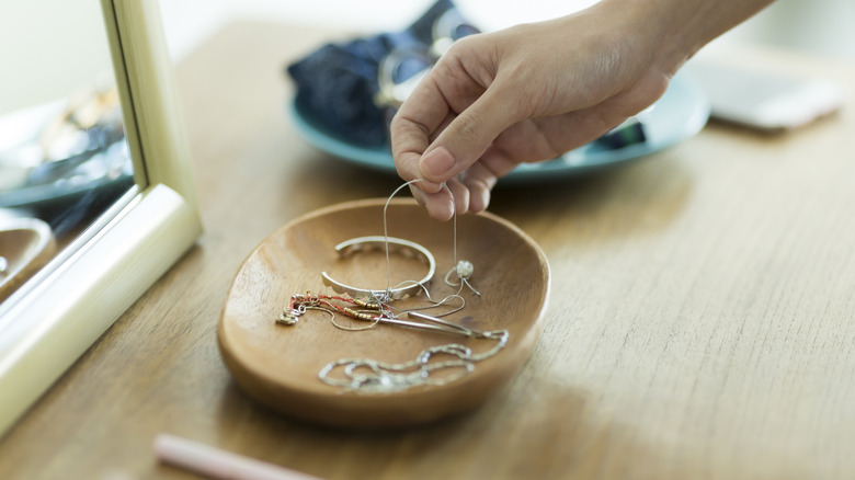 Hand placing a necklace in a small dish.
