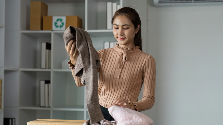 A young woman holds a sweater as she sorts through old clothes