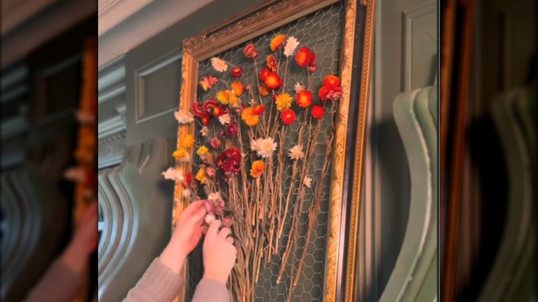 Person repurposing gold picture frame into flower wall decor with chicken wire