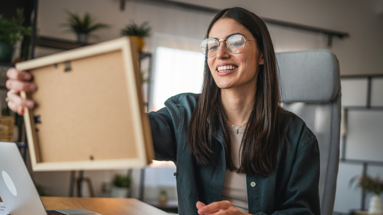 A woman smiles as she holds up a frame