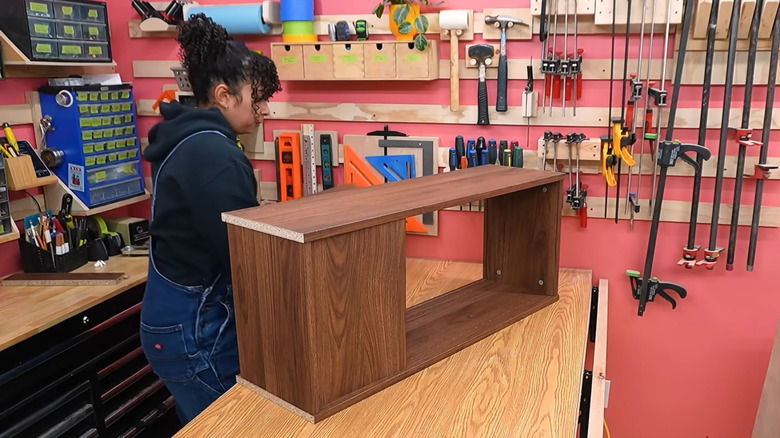 A woman assembles a walnut IKEA BILLY bookcase in a woodworking shop