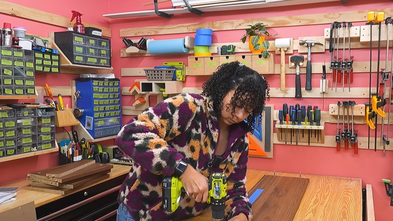 A woman in a colorful jacket drills into wood