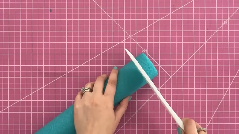 Person cutting a teal pool noodle on a pink cutting mat