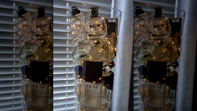 Glass vase filled with perfume bottles lit by LED light on window shelf