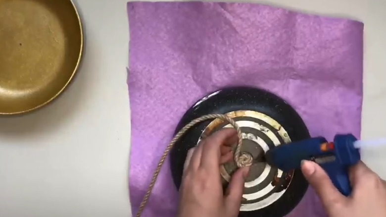 Woman hot-gluing jute rope to the bottom of an old frying pan for DIY countertop storage project