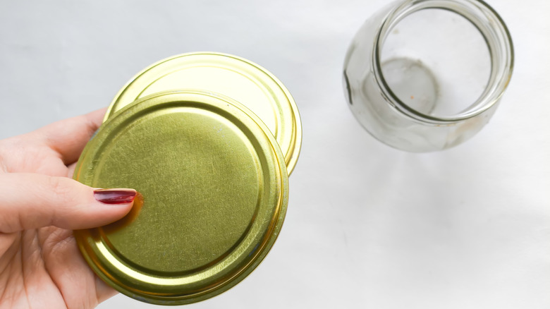 Hand holding jar lids and glass jar