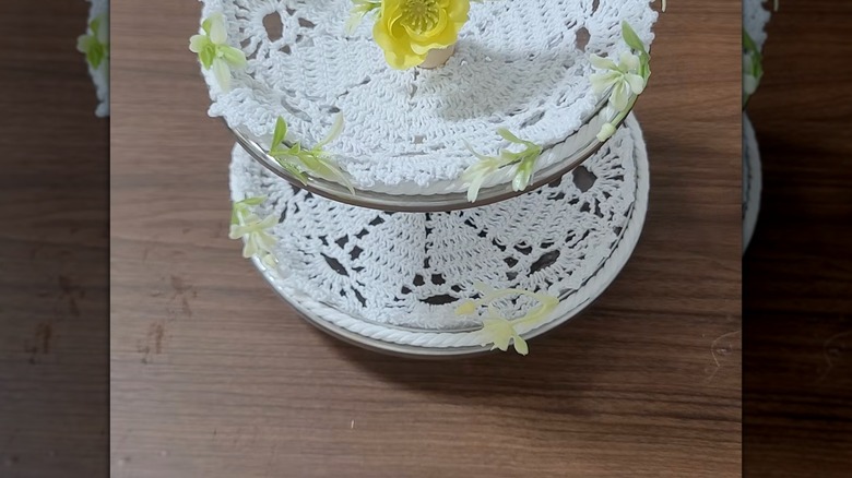 A tiered stand decorated with lace doilies and imitation flowers