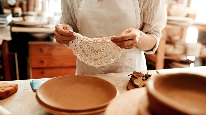 A person in an apron holding a lace doily