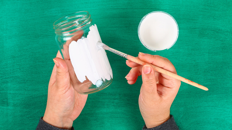 A person painting a jar white
