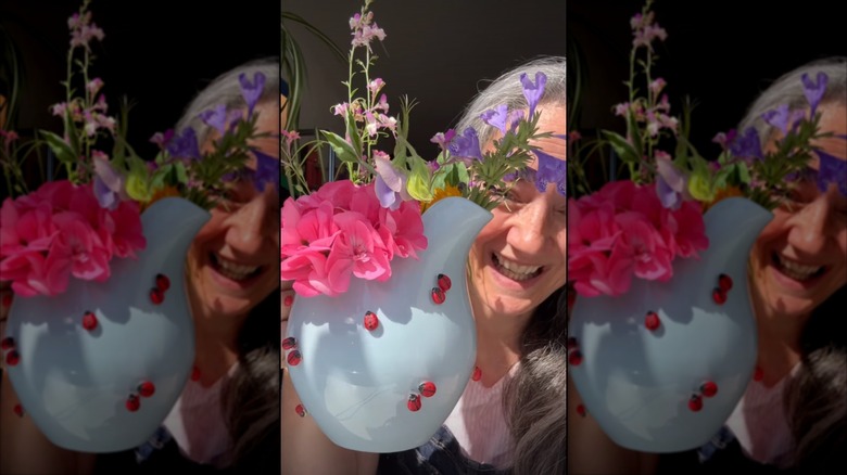 A woman holding a pitcher full of flowers and covered in popcorn kernel ladybugs