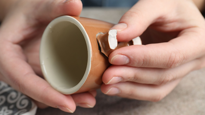 Close-up of hands inspecting ceramic mug with broken-off handle