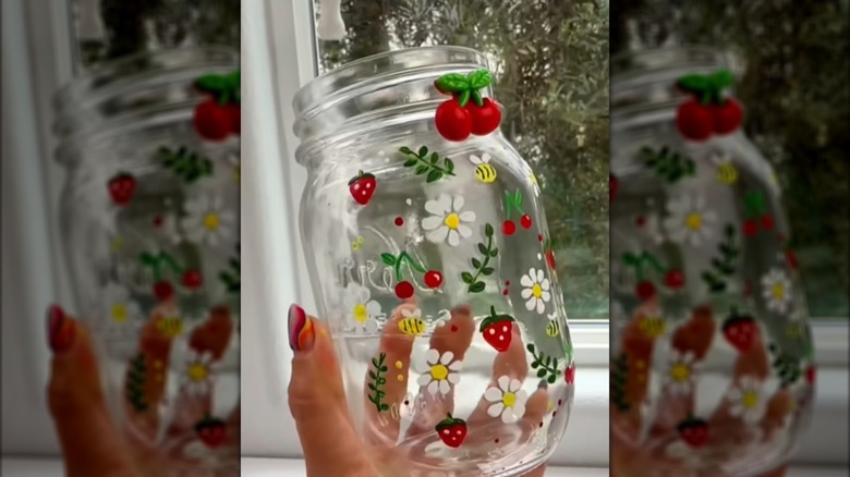 Creator holding up a Mason jar painted with leaves, flowers, bees, and fruit
