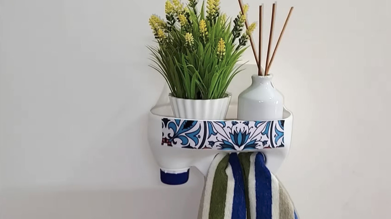 DIY mounted milk jug organizer holding towel, with decor on top.