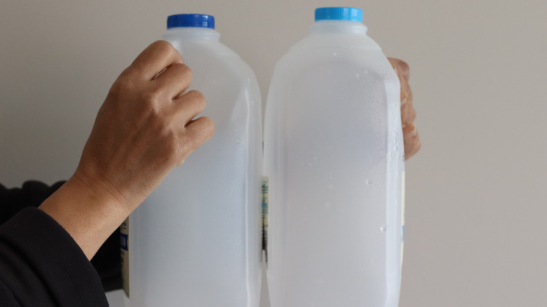 Person holding up empty milk jugs.